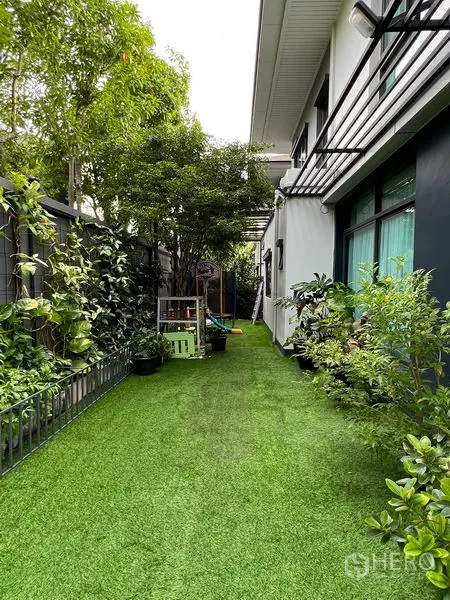 Detached House for sale in Bang Kapi, Bangkok - Lush side yard with artificial grass, potted plants and a walkway along the house.