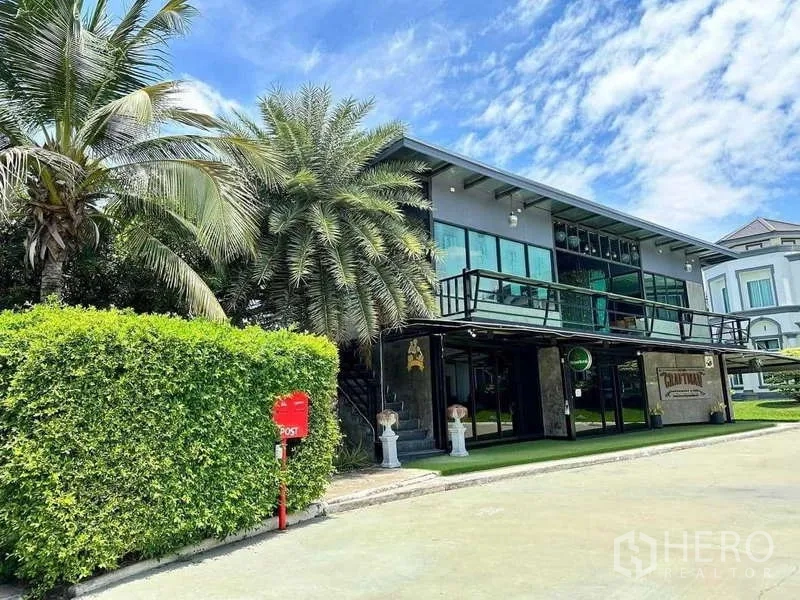 Detached House for sale in Khlong Luang, Pathum Thani - Contemporary pavilion with wraparound balcony beside palm trees and hedges.