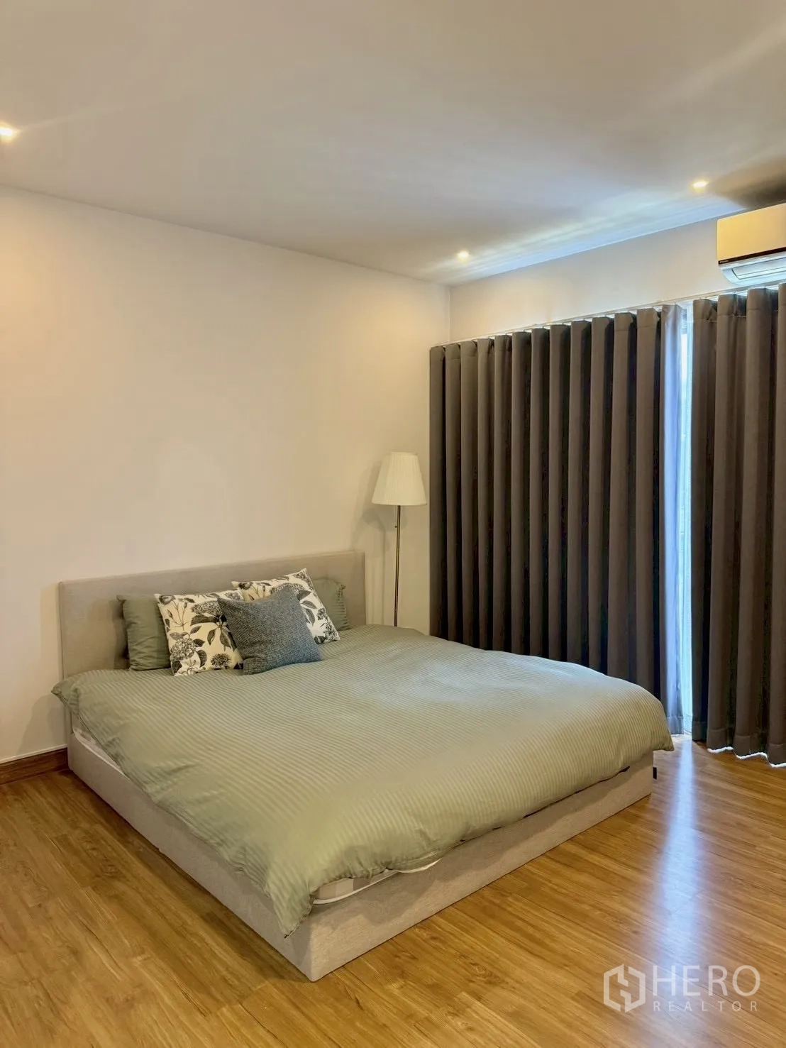 Townhouse for rent in Prawet, Bangkok - Primary bedroom with double bed, floor lamp, dark drapes and wood floors.