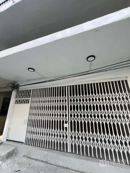 Shophouse for rent in Watthana, Bangkok - White shophouse facade with folding metal security gate and canopy lighting.