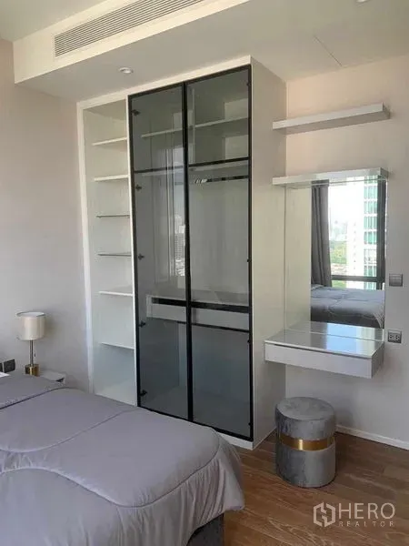 Condominium for rent in Pathum Wan, Bangkok - Built‑in glass wardrobe with open shelves and vanity in a contemporary Bangkok condominium bedroom.