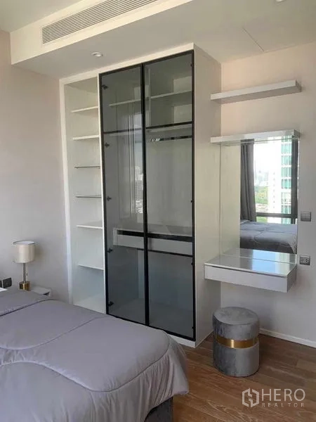Condominium for rent in Pathum Wan, Bangkok - Built‑in glass wardrobe with open shelves and vanity in a contemporary Bangkok condominium bedroom.
