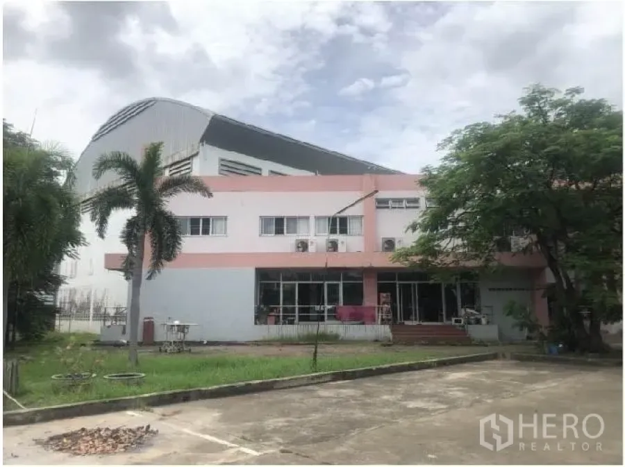 Warehouse for rent in Saphan Sung, Bangkok - Two-storey office building in front of a large warehouse with parking and greenery.