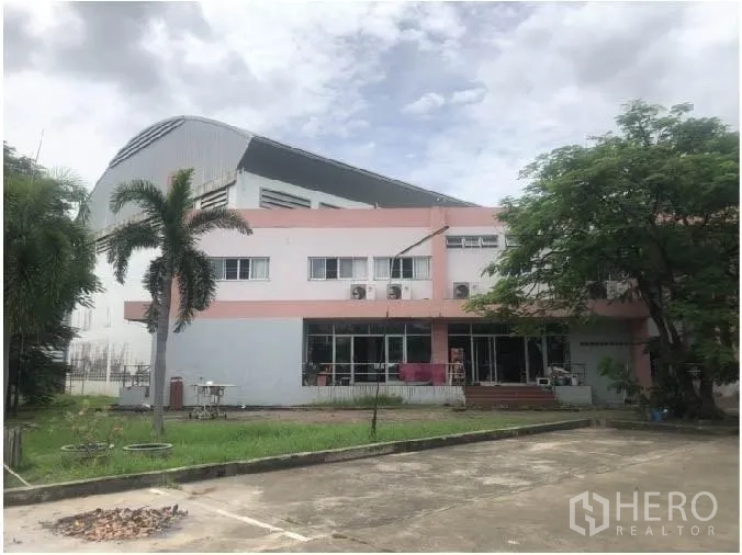 Warehouse for rent in Saphan Sung, Bangkok - Two-storey office building in front of a large warehouse with parking and greenery.