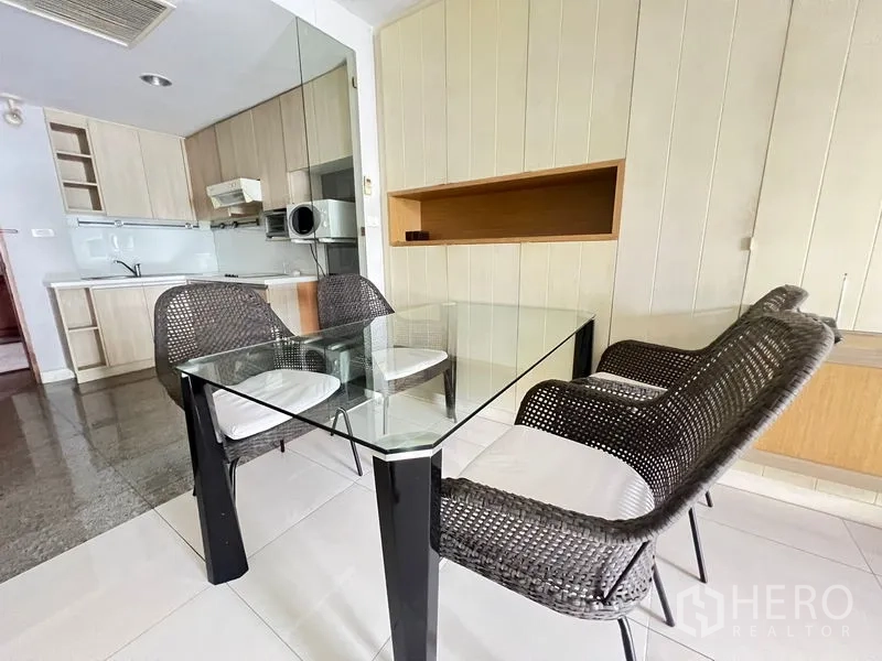 Condominium for rent or sale in Khlong Toei, Bangkok - Glass dining table with woven chairs next to the compact kitchen.