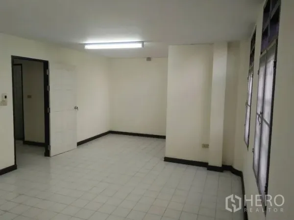 Townhouse for rent in Phra Khanong, Bangkok - Spacious tiled living area with fluorescent ceiling light and a row of windows.