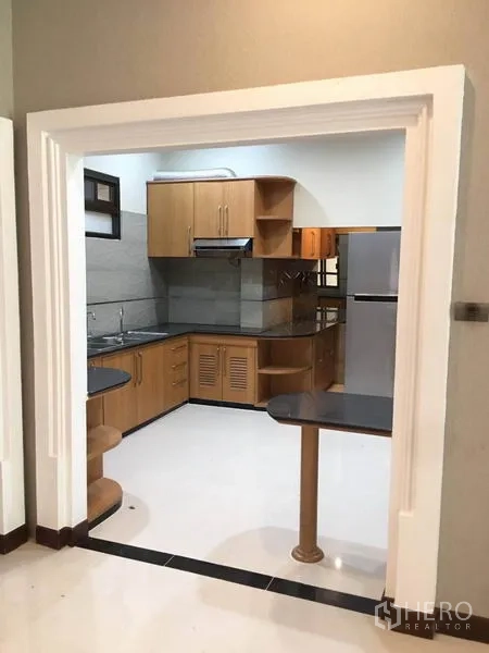 Detached House for rent in Khlong Toei, Bangkok - Separate kitchen with wood cabinets, stone countertops and stainless-steel fridge.