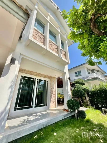 Detached House for sale in Prawet, Bangkok - Side garden and facade of a two-storey house with stone accents and sliding doors.