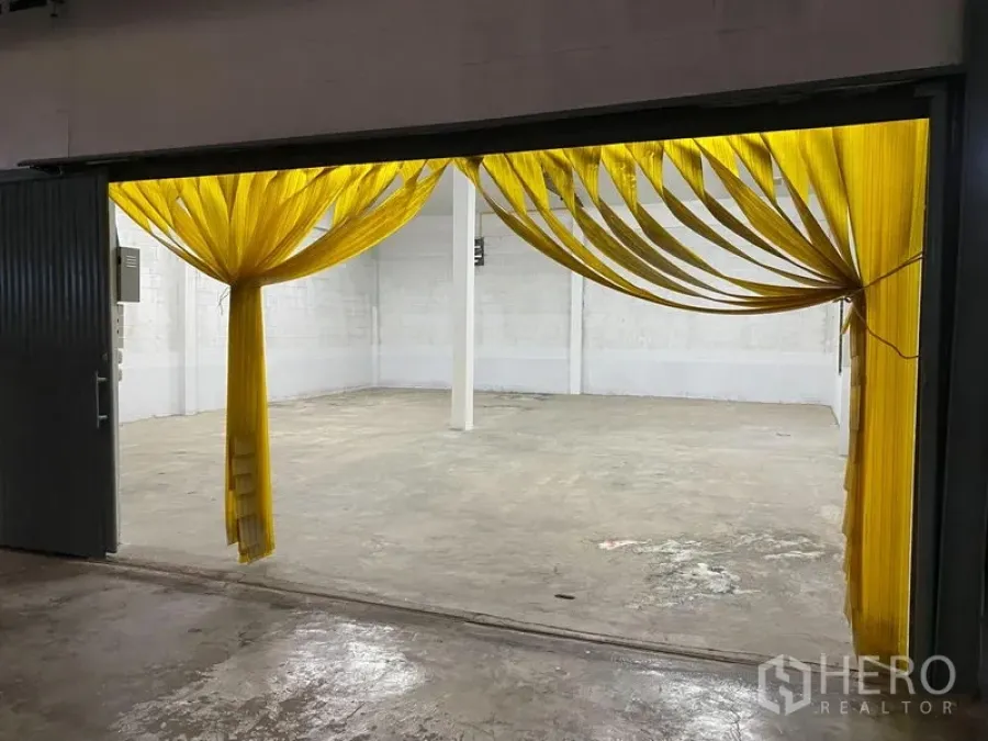 Warehouse for rent - Wide loading entrance with yellow PVC strip curtains revealing a clean warehouse space with concrete flooring and a central support column.