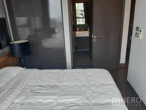 Condominium for rent or sale in Khlong Toei, Bangkok - Bedroom with built-in wardrobe and doorway leading to the bathroom.