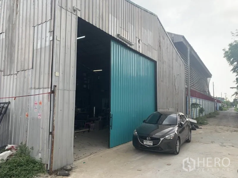 Warehouse for rent in Bang Kapi, Bangkok - Metal-clad warehouse exterior with wide teal sliding door and driveway parking in Bang Kapi.
