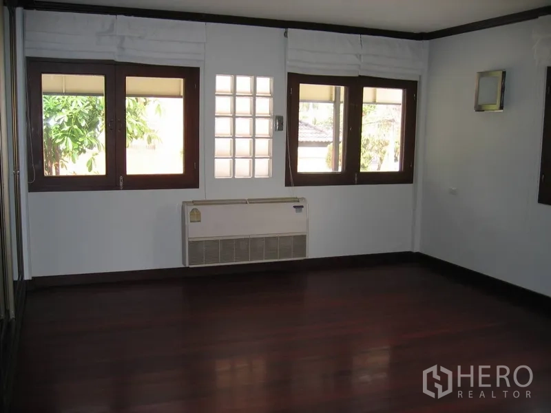 Detached House for rent in Watthana, Bangkok - Bright bedroom with multiple wood-trim windows and a wall AC unit.