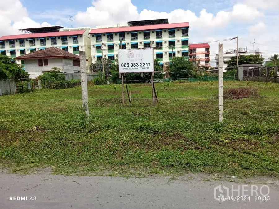 地 出租在Khan Na Yao, Bangkok - 带围栏的草地空地，立有出租标识，后方为低层公寓，位于康那耀区。