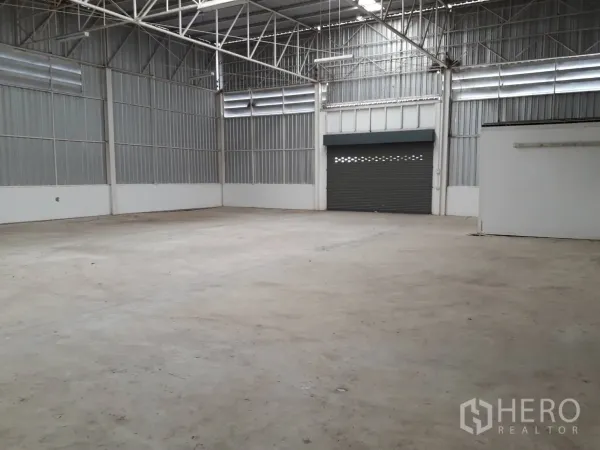 Warehouse for rent or sale in Khlong Luang, Pathum Thani - Spacious warehouse interior with concrete floor, high steel truss roof and a roller shutter door.