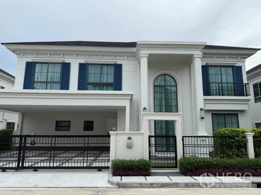 Detached House for rent or sale in Bang Phli, Samut Prakan - Front exterior of a two-storey modern classic house with blue shutters, arched entry and a gated carport.