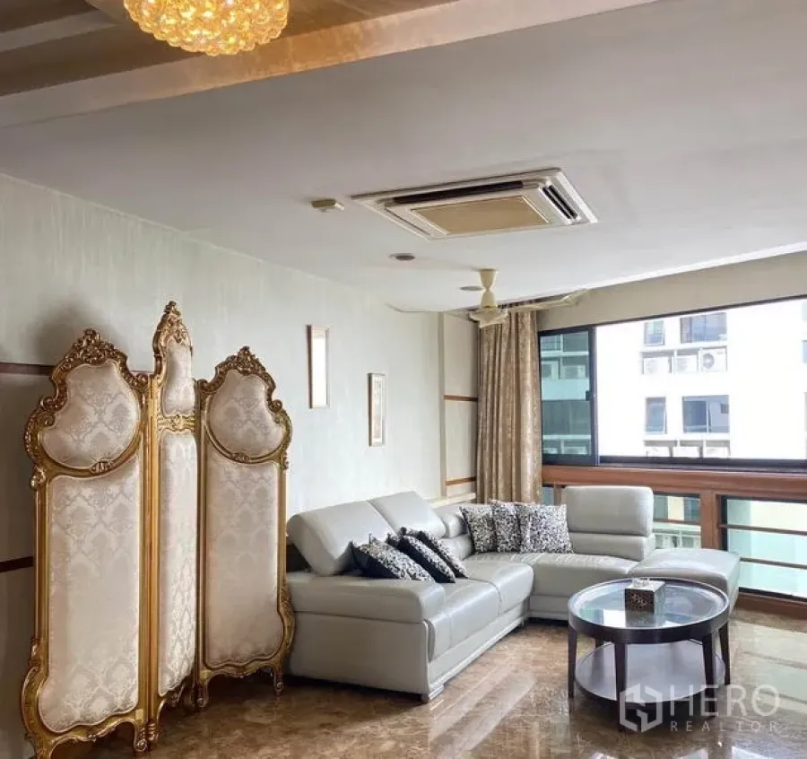 Condominium for rent in Khlong Toei, Bangkok - Sitting area with sectional sofa, ornate gold screen and wide windows.