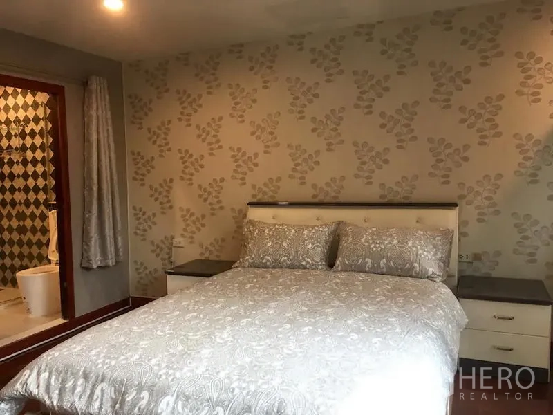 Townhouse for rent in Bang Rak, Bangkok - Bedroom with patterned wallpaper, queen bed, bedside cabinets and en-suite bathroom entry.