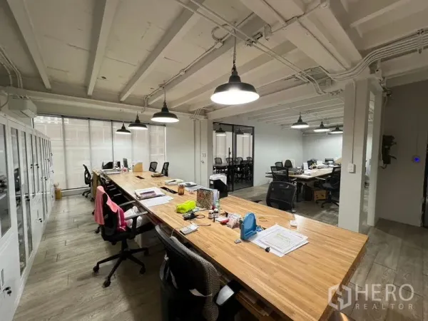 办公空间 出租在Pathum Wan, Bangkok - 开放式办公室，长木质工位、人体工学椅、大窗与外露天花照明。