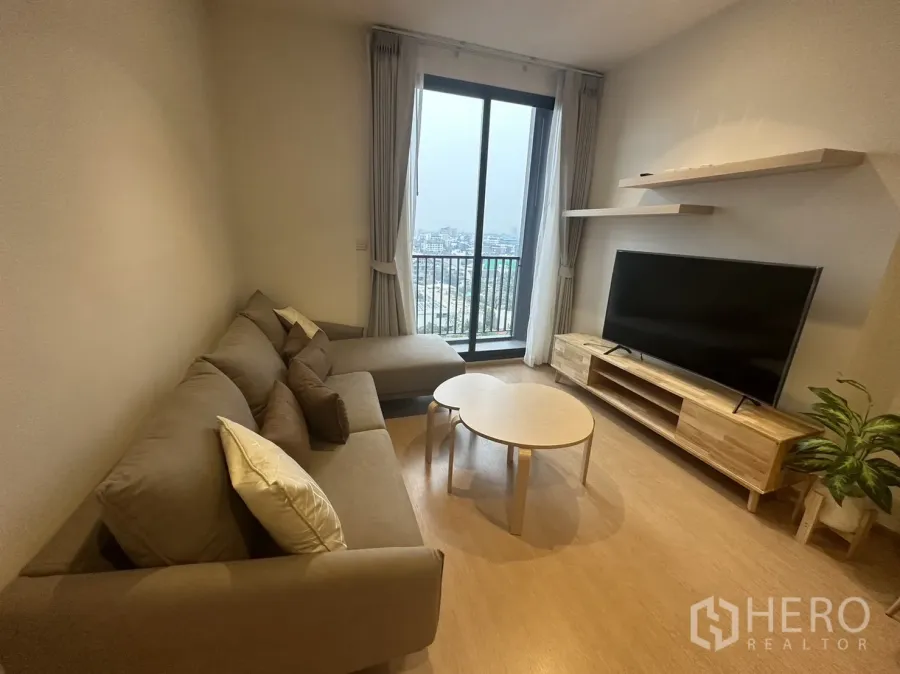 Condominium for rent in Watthana, Bangkok - Bright living room with L-shaped sofa, TV console and balcony city view.