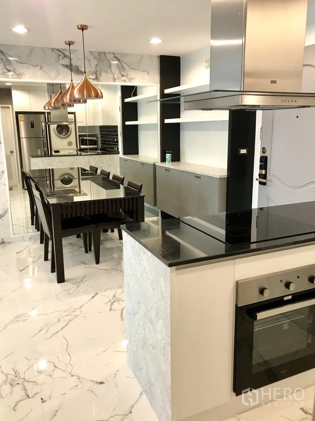 Condominium for rent or sale in Khlong Toei, Bangkok - Modern open kitchen and dining area with island cooktop, black stone countertop, oven and stainless hood.