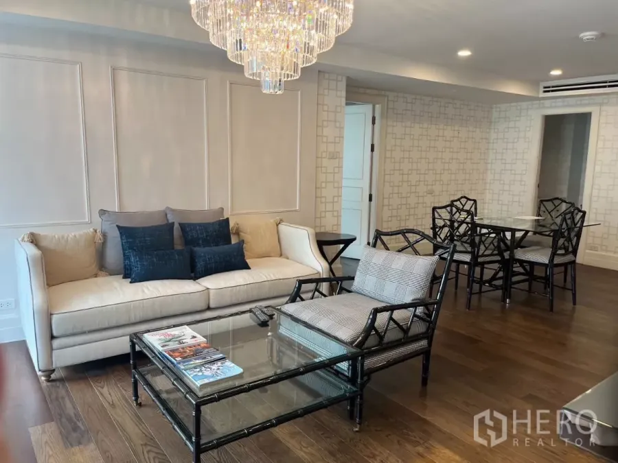 Condominium for rent in Pathum Wan, Bangkok - Elegant living room with cream sofa, glass coffee table, and crystal chandelier on dark wood floors.