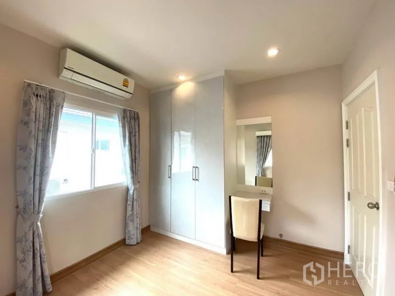 Detached House for rent in Suan Luang, Bangkok - Third bedroom with glossy built-in wardrobe, window, air-conditioner and vanity.