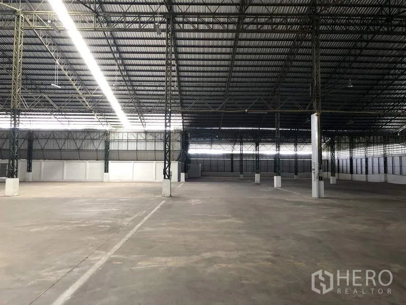Warehouse for rent in Mueang Pathum Thani, Pathum Thani - Empty warehouse hall with marked drive lanes, high ceiling and ventilated side panels for airflow.