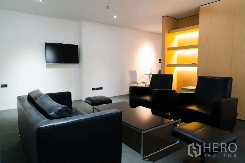 Office Space for rent - Lounge area with black leather sofas, wall-mounted TV and illuminated shelving.