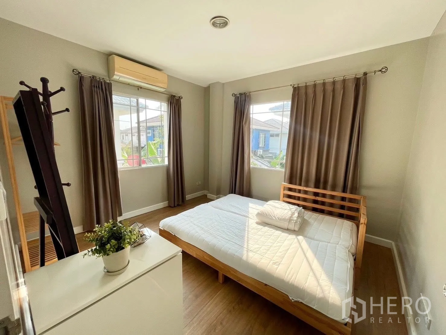 Detached House for rent in Prawet, Bangkok - Sunlit bedroom with wooden bed, dresser, curtains and wall air conditioner.