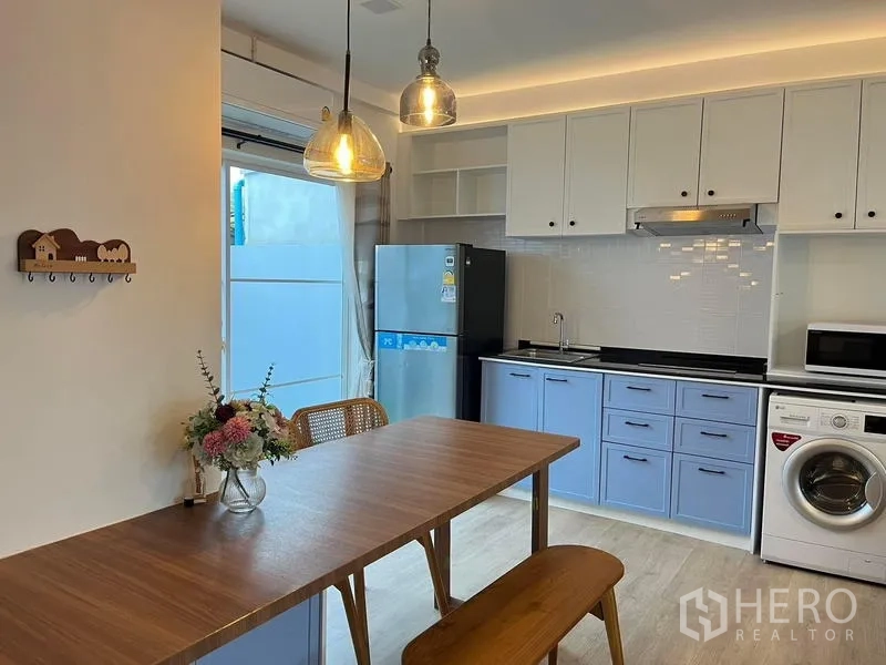 Townhouse for rent in Prawet, Bangkok - Modern kitchen with blue and white cabinetry, tiled backsplash, fridge, range hood, and washing machine.
