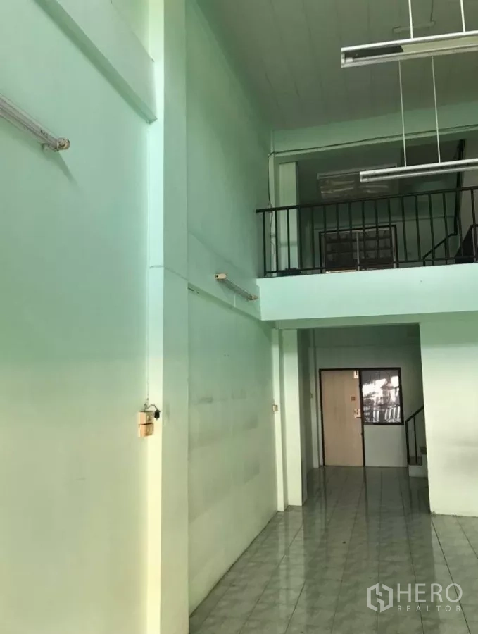 Shophouse for rent in Suan Luang, Bangkok - High-ceiling shop space showing mezzanine railing and fluorescent fixtures.