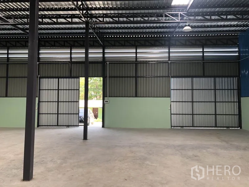 Warehouse for rent in Khlong Luang, Pathum Thani - Spacious warehouse interior with high steel truss roof, concrete floor and large sliding gates.