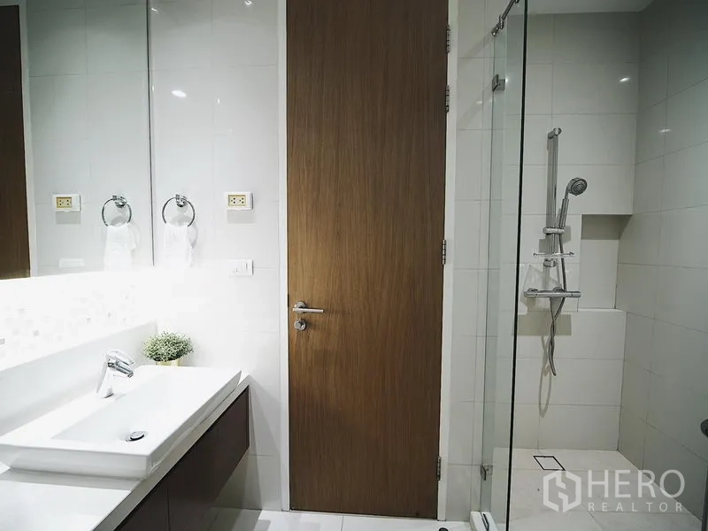 Condominium for rent in Khlong Toei, Bangkok - Second bathroom with glass-enclosed rainfall shower and bright vanity.