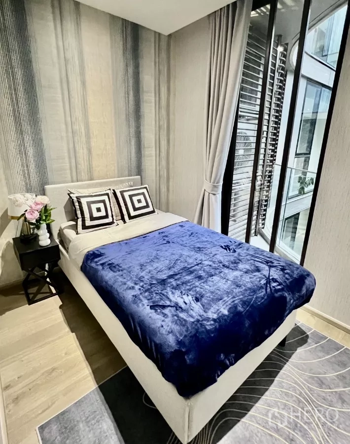 Condominium for rent in Khlong Toei, Bangkok - Second bedroom with blue blanket and full-height glazing.