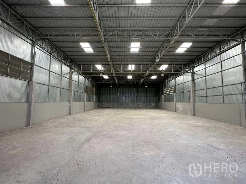 Warehouse for rent in Mueang Pathum Thani, Pathum Thani - Empty open-plan storage bay with metal walls, bright roof panels and even floor.