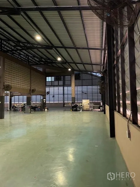 Warehouse for rent in Si Racha, Chon Buri - Work area beside louvered windows with wall-mounted fans and epoxy flooring.