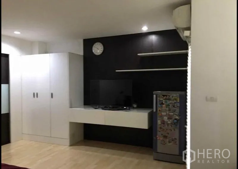 Townhouse for sale in Khlong Toei, Bangkok - Contemporary room showing TV, open shelves and compact fridge against a dark feature wall.