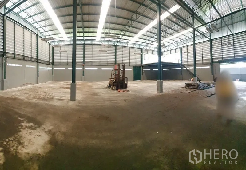 Factory for rent in Saphan Sung, Bangkok - Large clear‑span factory floor under skylights with steel columns, forklift and a mezzanine platform.