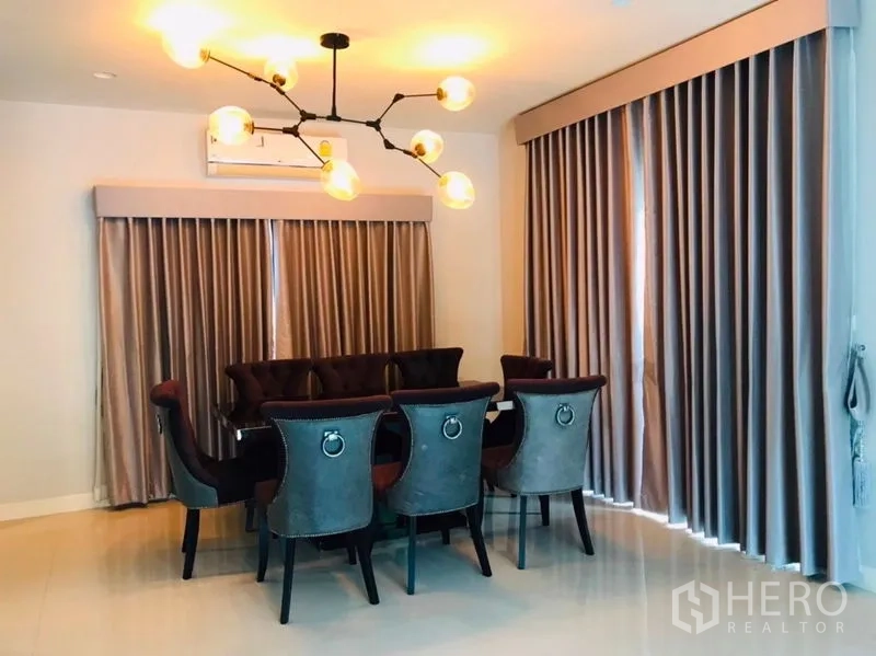 Detached House for rent or sale in Pathum Thani - Dining room with eight-seat table, statement chandelier and long curtains.