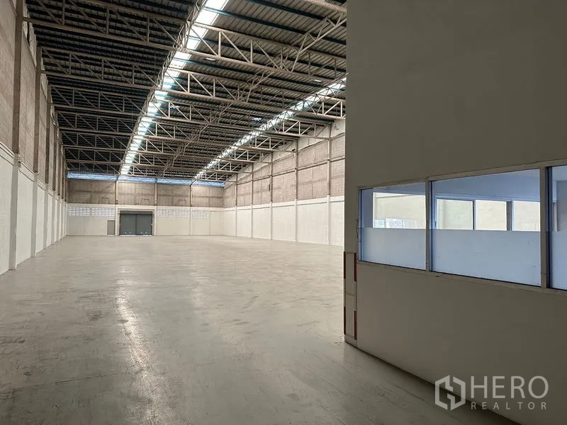 Factory for rent in Si Racha, Chon Buri - Warehouse interior viewed beside office windows and doorway, showing clear-span floor.
