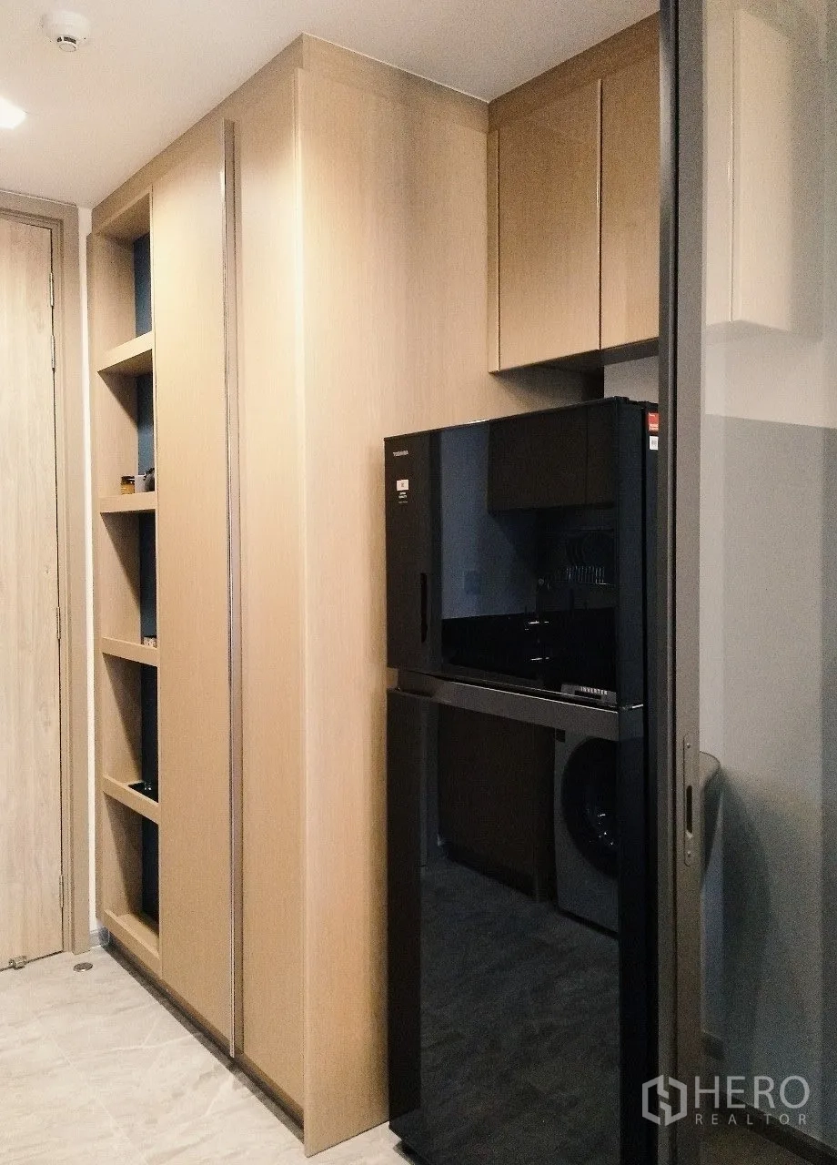 Condominium for rent in Watthana, Bangkok - Kitchen area with black refrigerator and built-in cabinetry beside a glass partition.