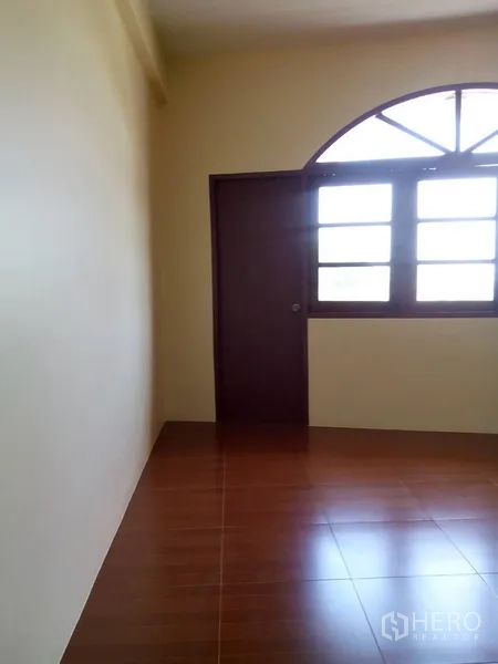 Shophouse for rent in Phra Khanong, Bangkok - Empty room with brown floor tiles, wooden door and an arched window.