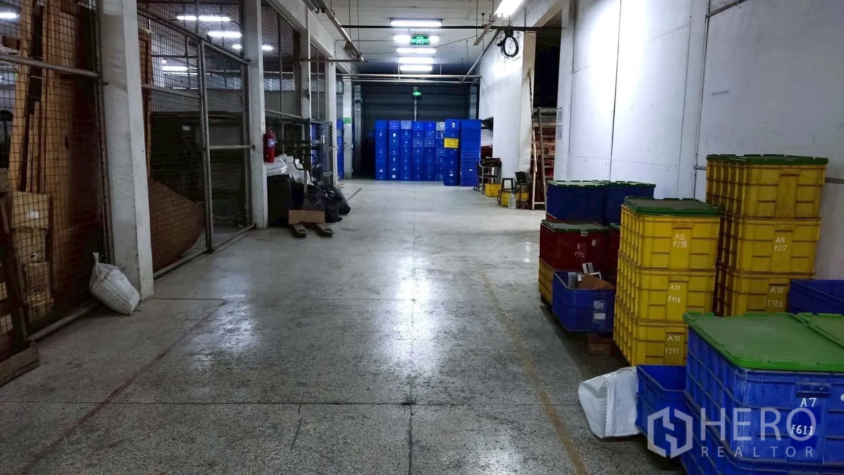 Factory for sale in Lat Krabang, Bangkok - Storage aisle with wire-mesh cages and stacks of plastic crates near a roller door.