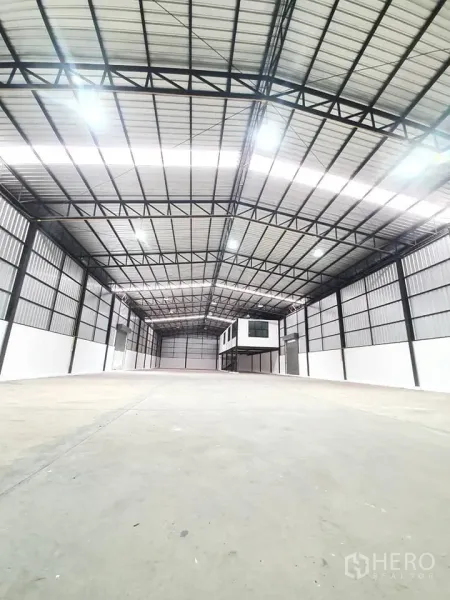 Warehouse for rent in Bang Khen, Bangkok - Clear-span storage hall with bright lighting and elevated box-style office at the far end.