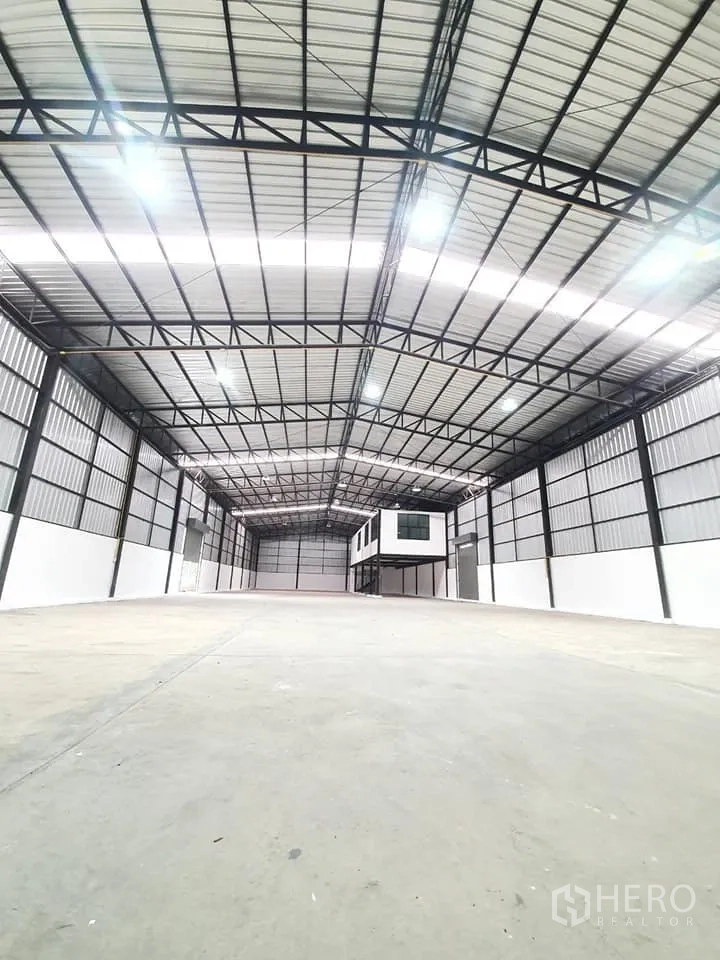 Warehouse for rent in Bang Khen, Bangkok - Clear-span storage hall with bright lighting and elevated box-style office at the far end.
