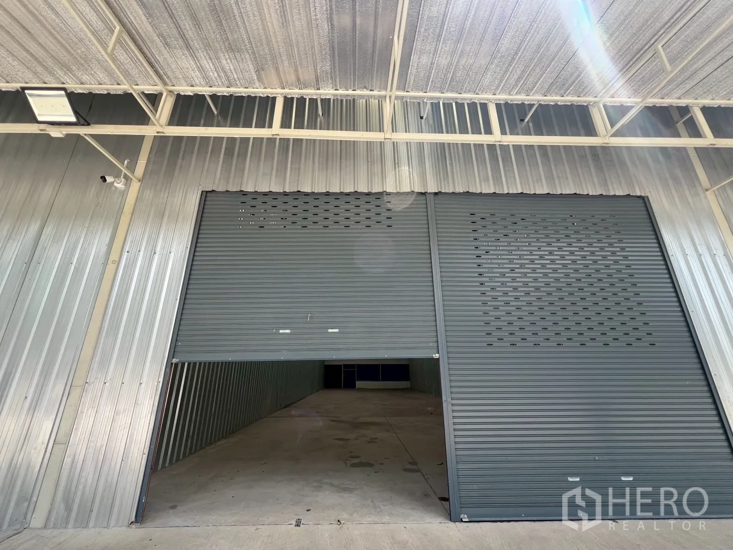 Warehouse for rent in Min Buri, Bangkok - Close view of the warehouse entrance showing a partially open steel roller shutter beneath a canopy for loading.