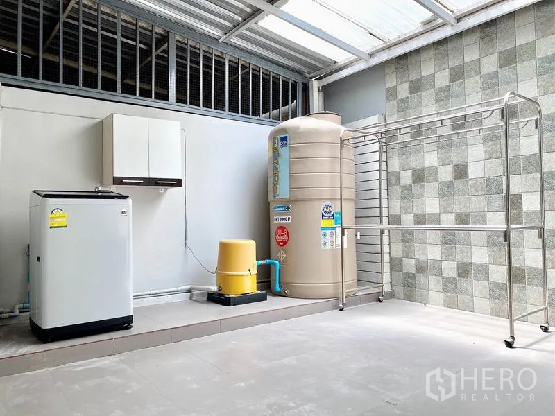 Townhouse for rent in Prawet, Bangkok - Laundry zone with washing machine, water tank, pump and stainless drying rack under roof.