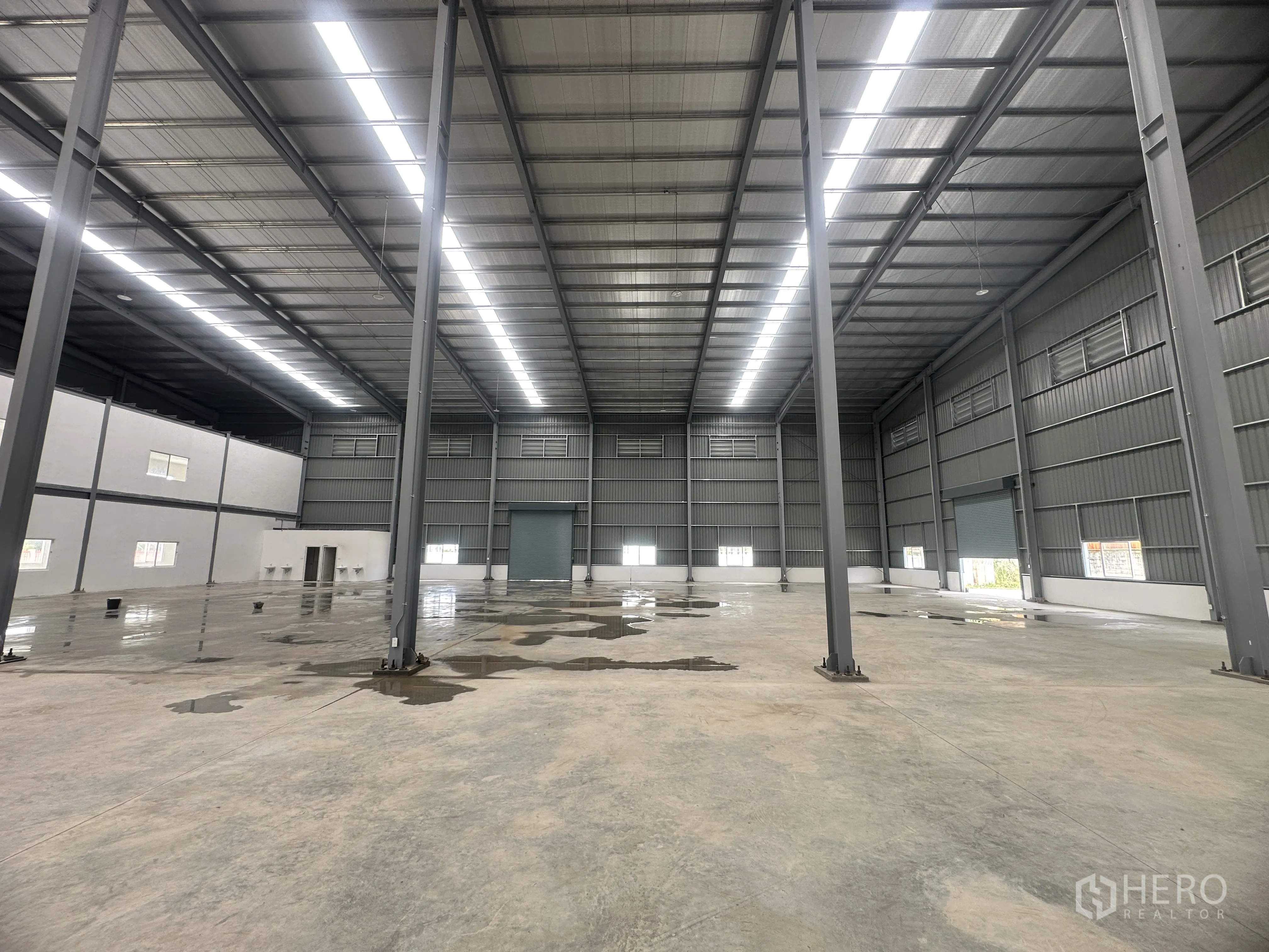 Warehouse for rent or sale in Lam Luk Ka, Pathum Thani - Spacious warehouse interior with tall steel columns, skylight roof strips, concrete floor, and an internal office block.