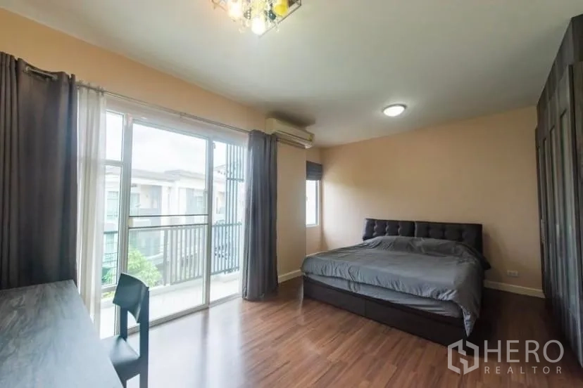 Townhouse for rent in Suan Luang, Bangkok - Bright master bedroom with wood floors, balcony access, large windows and built-in wardrobe.