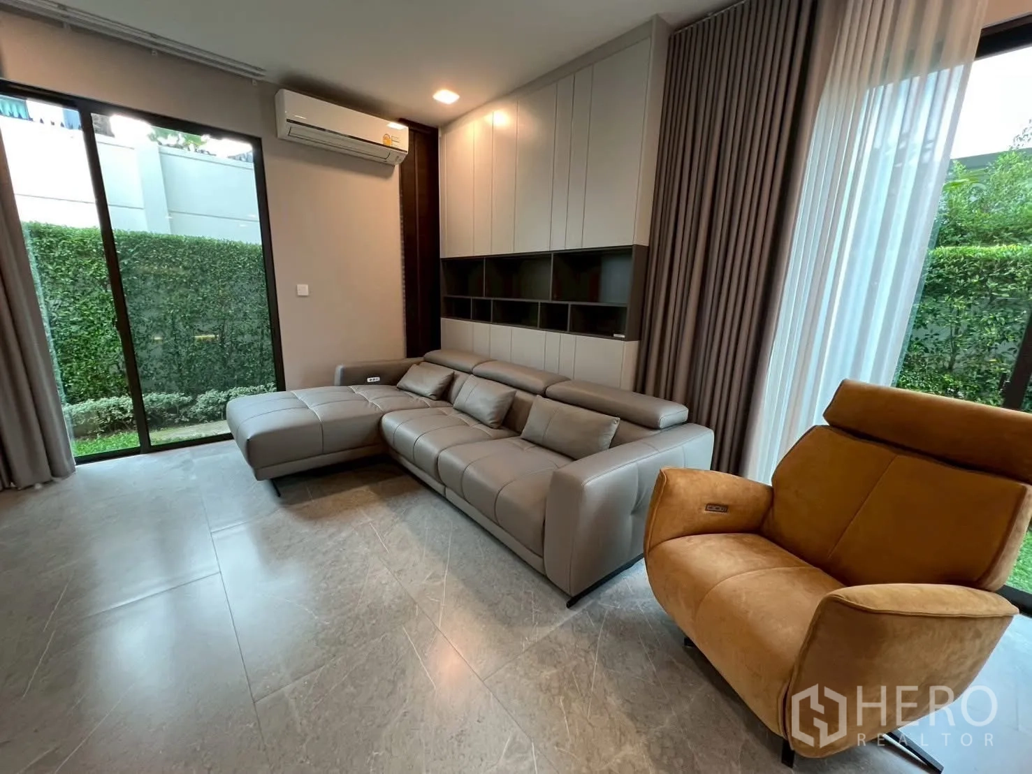 Detached House for rent in Samut Prakan - Cozy living corner with sectional sofa, built-in shelving, and large windows.